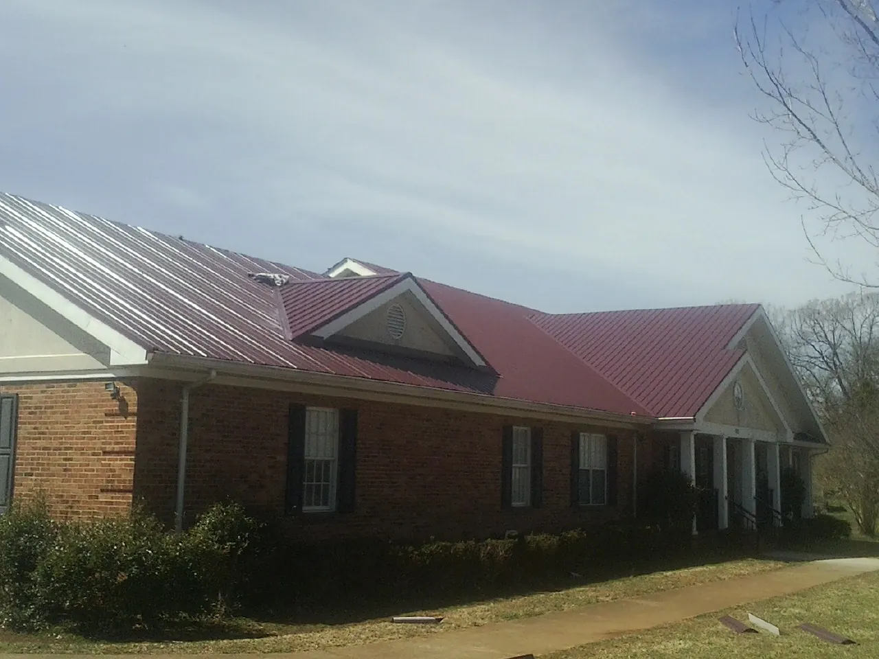 Red metal roof with gabled entries on a long brick building, from a Hail Damage Roof Repair job in Pine Mountain