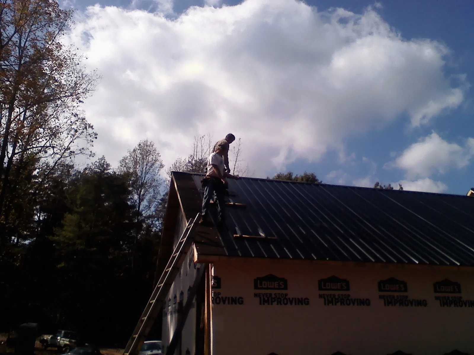 Roofer fastening dark metal panels high against a cloudy sky, from a Roof Inspection job in Pine Mountain